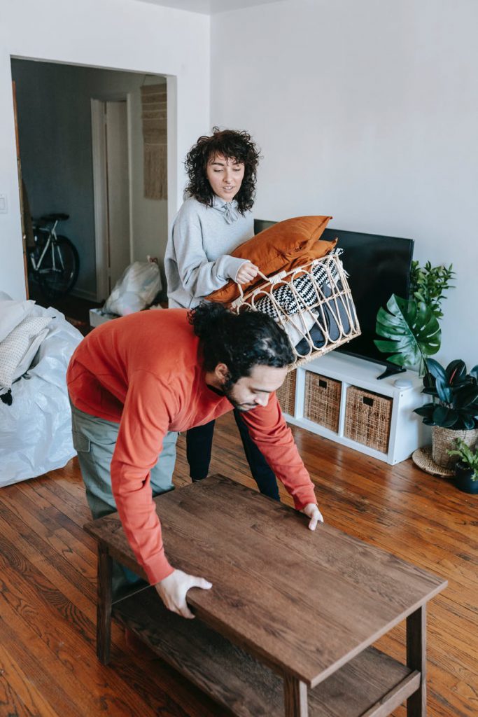 woman carrying a basket of pillows and a man lifting a table